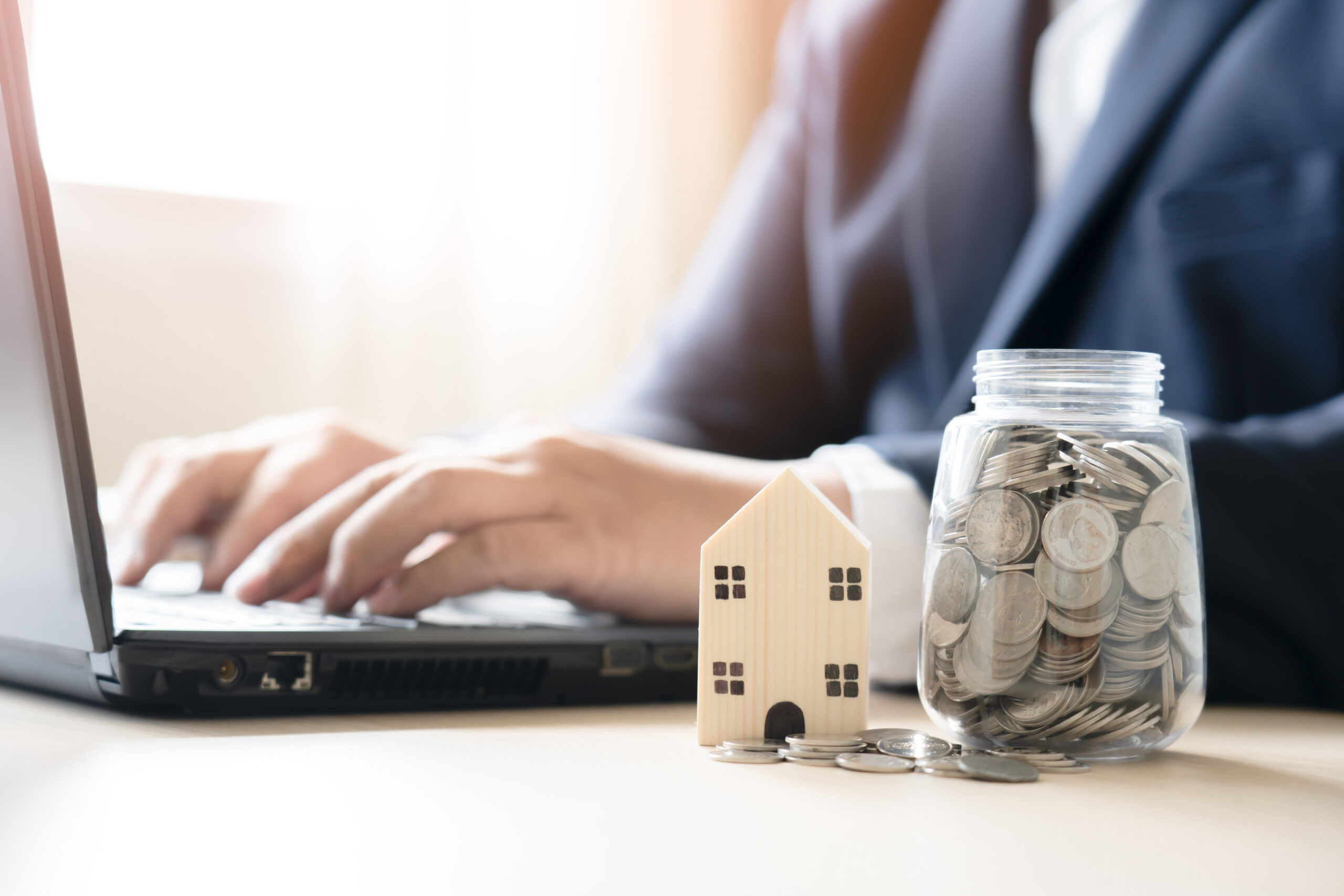 Business man working with laptop savings money Thai currency coins in jar for house